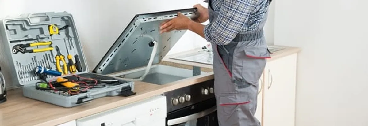 Cooktop repair technician lifting a built-in stovetop for service in Denver, CO