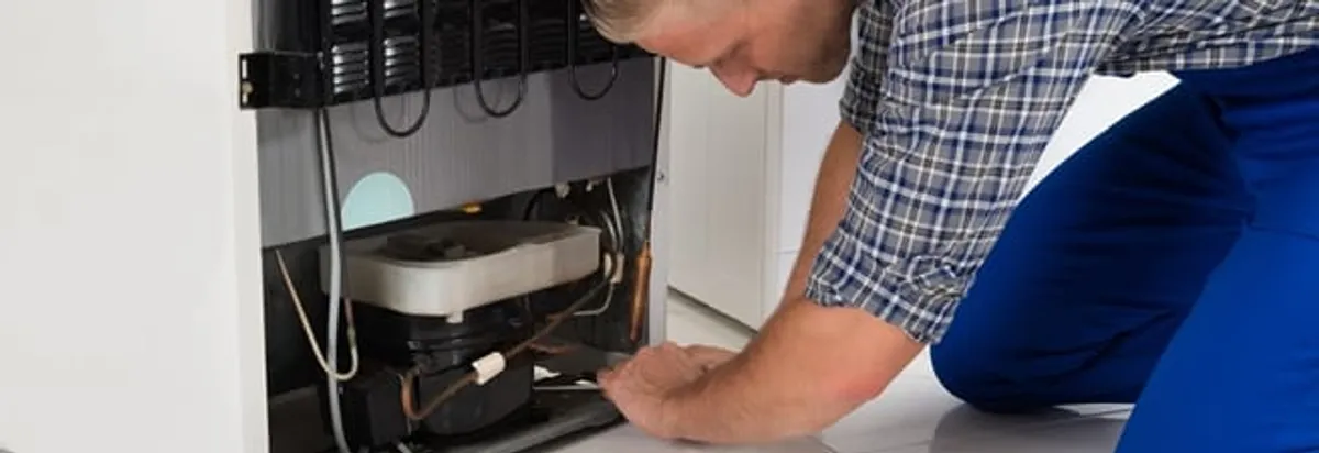 Refrigerator repair technician servicing the compressor and condenser area in Denver, CO