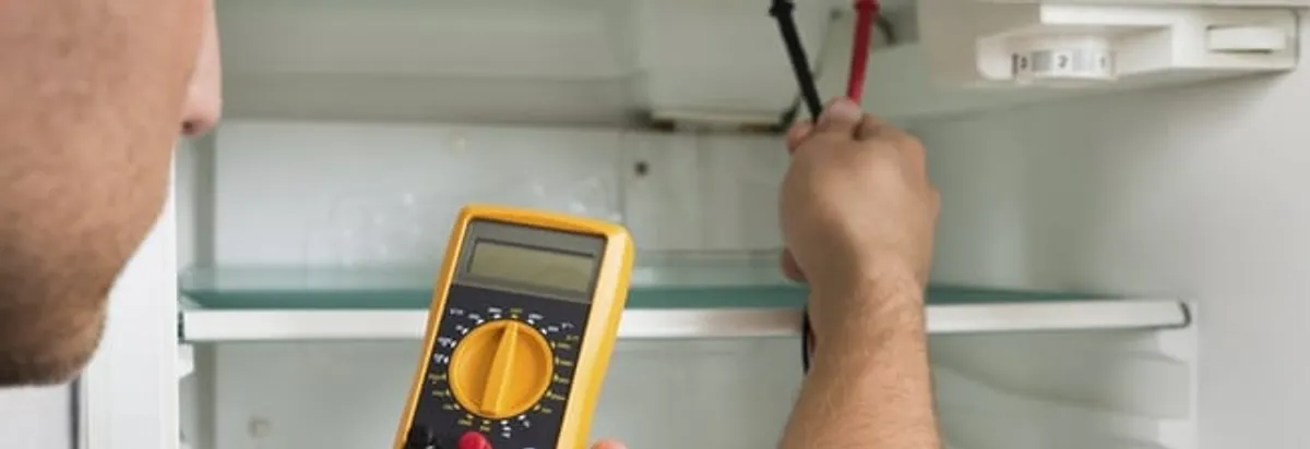 Refrigerator repair technician testing electrical components with a multimeter in Denver, CO